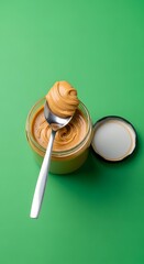 A jar of creamy peanut butter with a spoon resting inside, set against a vibrant green background for a fresh and inviting presentation