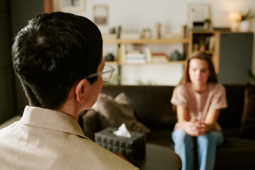 Middle aged Caucasian woman with short hair and glasses sitting across from young adult Caucasian woman with long hair, discussing mental health issues in therapy session