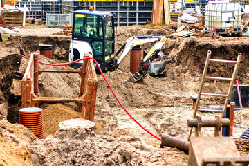 Active urban construction site showing foundation work with a mini-excavator, rebar, concrete...