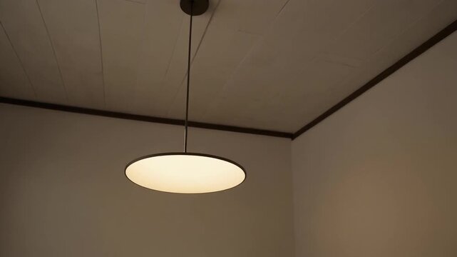 Contemporary circular ceiling lamp casting a soft glow in a minimalist room corner, showcasing modern interior lighting design and a serene atmosphere