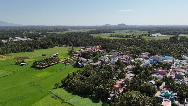 Aerial footage of a cellophane towers with Vibrant rooftops meet endless greenery in this stunning aerial view of a tropical South Indian town surrounded by palm trees and fertile fields.