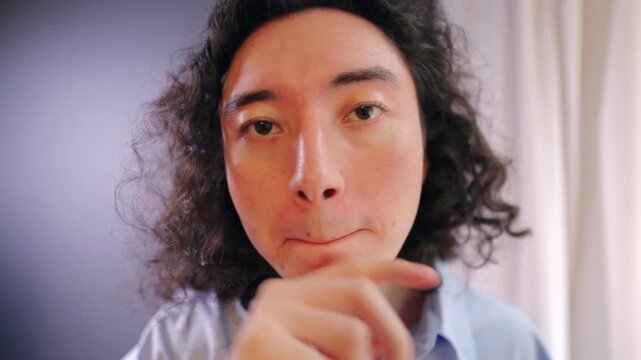 Close up video portrait of young asian man touching face and looking directly at camera. Concept of self reflection, concentration, emotions and body language in modern business or lifestyle context