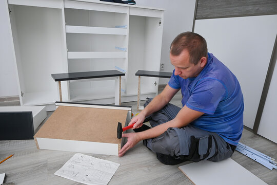 Man assembling and installing new diy furniture at home using a hammer and instructions