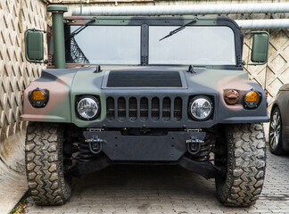 Naklejka premium Military Humvee parked on an street, showcasing its rugged design and operational readiness in a secure military base. Khaki camouflage military Hummer front view. Army USA. 