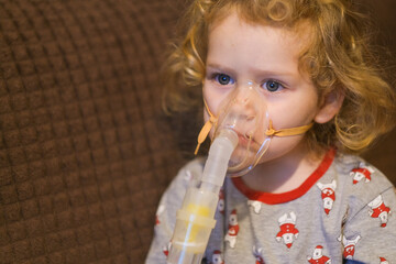 Little child with curly hair and blue eyes undergoing medical treatment with nebulizer mask. Pediatric healthcare for respiratory illness.