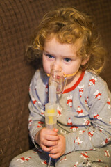 Little kid with curly hair receiving respiratory therapy through medical nebulizer mask. Medicine and healthcare concept for child illness treatment.