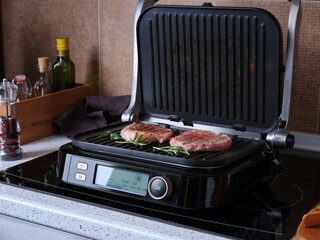 A marbled beef steaks grilling on an electric grill against the backdrop of a home kitchen.