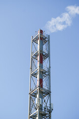 Industrial red and white chimney emitting smoke into a clear blue sky. Concept of environmental pollution, factory operations, and energy production.