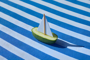 きゅうりボートと紙のセイルが乗ったミニマルフードアート、マリンボーダー背景の夏コンセプトとコピースペース