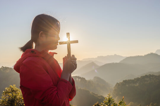 Girl praying and holding Christian cross for worshipping God on mountain at sunrise background. Christian, Christianity, Religion copy space background. Easter Sunday concept: - Powered by Adobe