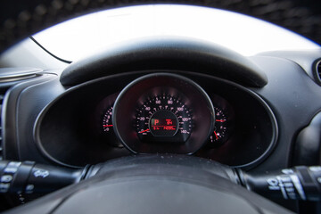 Instrument cluster of a 2017 red South Korean hatchback car showing speedometer fuel gauge and digital display through steering wheel view in daylight. Great for automotive marketing and blogs