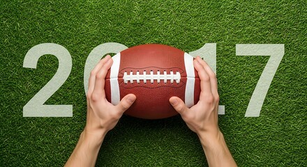 Hands holding american football over green grass with the year 2017 displayed