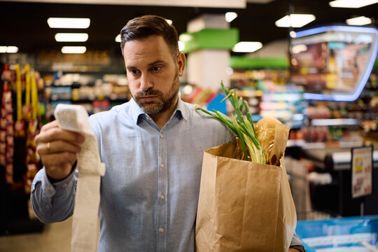 Worried man checking the bill after buying groceries at supermarket.