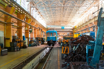 A blue train is positioned inside a large maintenance facility. Tools and materials are organized around the workshop, highlighting the industrial atmosphere of train repairs