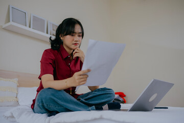 Serious asian woman sit on bed, check household bills, makes online payment using e-bank laptop...