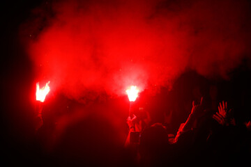 A group of people are holding red torches and are surrounded by smoke
