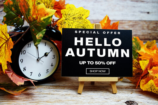 Hello Autumn Sale 50% off Special Offer text with alarm clock and maple leaf decoration on wooden background