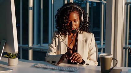 Typing woman in office wears headset. Businesswoman types on keyboard. Professional at desk near window. Woman adjusts headset during call. Morning light shows focused face. Focus on virtual call. - Powered by Adobe