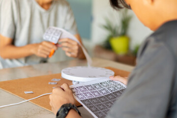 A person cuts out AR markers (ArUco codes) to prepare a white motorized turntable for smartphone photogrammetry or 3D scanning.
