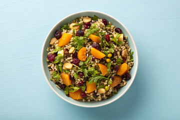 Healthy grain salad with fruit and nuts in a white bowl overhead view