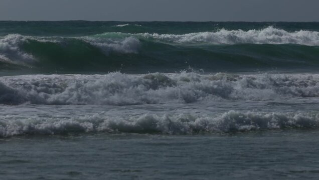 Dark teal ocean waves rolling toward the shore under a clear evening sky, capturing the raw power, texture and rhythm of the restless sea.