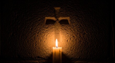 A single lit candle casting a warm glow on a textured wall with a shadow resembling a cross or religious symbol behind it
