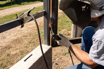 Male adult welding metal frame outdoors with protective gear. National Welding Month