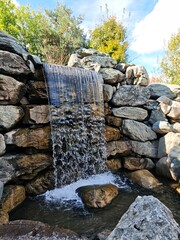 an artificial waterfall in a park against the backdrop of a stone wall