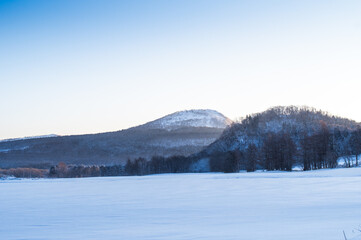 快晴の空の下の雪に覆われた野原と山々の冬の風景。澄んだ空気を感じる開放感。