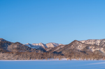快晴の空の下の雪に覆われた野原と山々の冬の風景。澄んだ空気を感じる開放感。