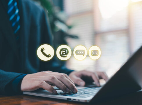 Businessman typing on a laptop with glowing contact icons including phone, email, chat, and message floating above the keyboard, symbolizing communication channels, customer support, online service.
