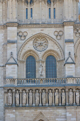 Detailed view of the Notre Dame Cathedral facade in Paris showing the statues of kings and ornate Gothic windows in sunlight.