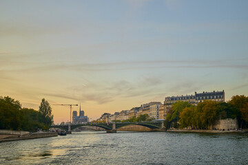 Obraz premium Wide view of the Seine River in Paris at sunset, showing bridges, classic Parisian buildings, and Notre Dame Cathedral in the distance.