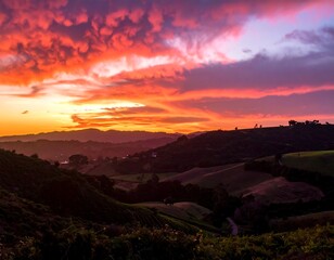 Fototapeta premium Dramatic fiery sunset illuminates rolling hills and valleys; vibrant colors paint the sky