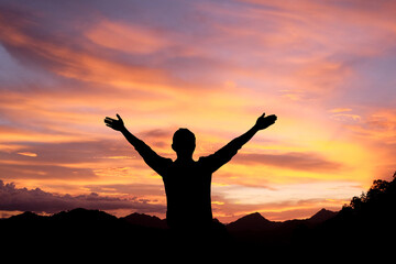 Silhouette of man with raised hands in the mountain at sunset