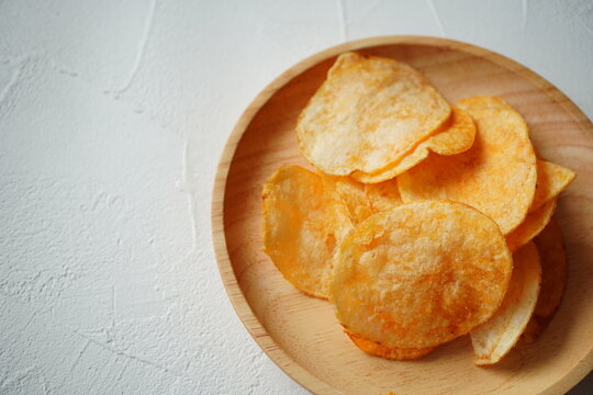 白い背景の上に置かれた木皿に、こんがりとしたポテトチップスを盛り付けた写真。シンプルで使いやすく、スナック広告・食べ物素材・食品パッケージ用のイメージにも適したフード写真。