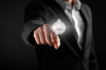 Professional hand pointing at a glowing power on/off button on a dark background. Concept of startup, activation, beginning, and energy control.