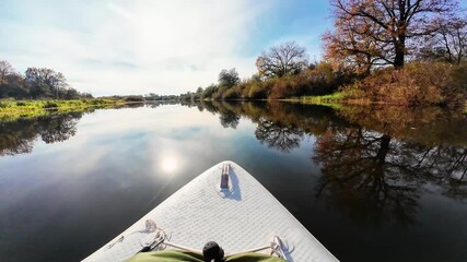 Indulge in a soothing paddleboarding experience on calm waters that beautifully reflect the vibrant autumn leaves, all beneath a clear and bright sky, making it an ideal escape for nature enthusiasts