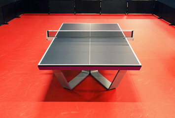 Black table tennis or pingpong table is settle on a red, orange floor of the indoor court stadium for competitions tournament