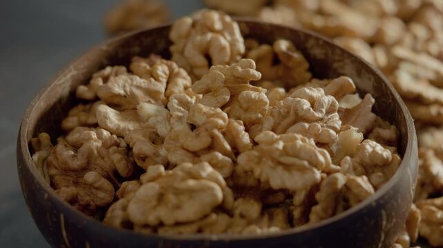 Discover the unique texture and flavor of walnut kernels displayed in a rustic wooden bowl, showcasing their natural beauty and freshness among scattered nuts.