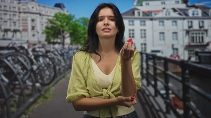 Young woman wearing a green blouse gestures with her hand and arm beside a canal on a city street; communication expression persuasion confidence.