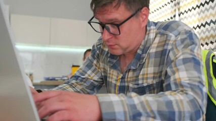 focused white technician troubleshooting laptop with intense typing and concentration, plaid shirt and glasses, workshop background with tools and colleagues, problem solving and software repair vibe