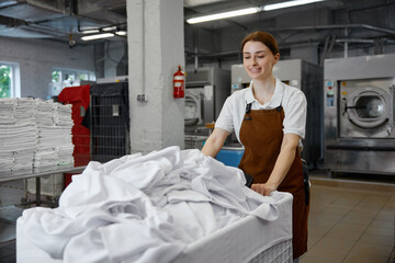A woman worker pushes a cart full of white sheets in a laundromat