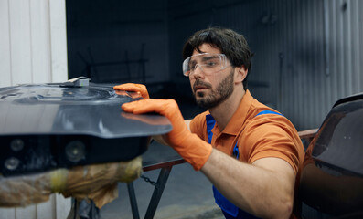 Technician worker skillfully restoring a car door in a busy garage workshop space