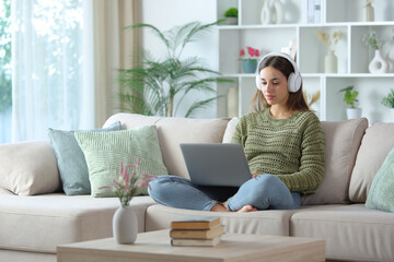 Serious woman in green wearing headphone using laptop