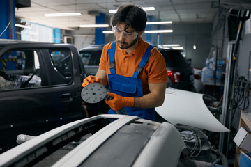 Auto body technician sanding car panel in workshop - repair and refinishing process