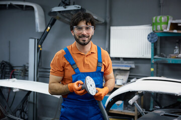An auto body technician is sanding and polishing a car inside a garage workshop environment