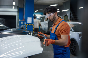 Auto body technician repairing car hood in professional garage workshop with safety gear