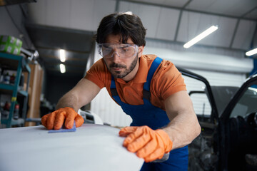 Auto body technician sanding car panel in workshop