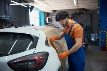 Automotive technician prepping compact car in garage for paint and bodywork refinishing